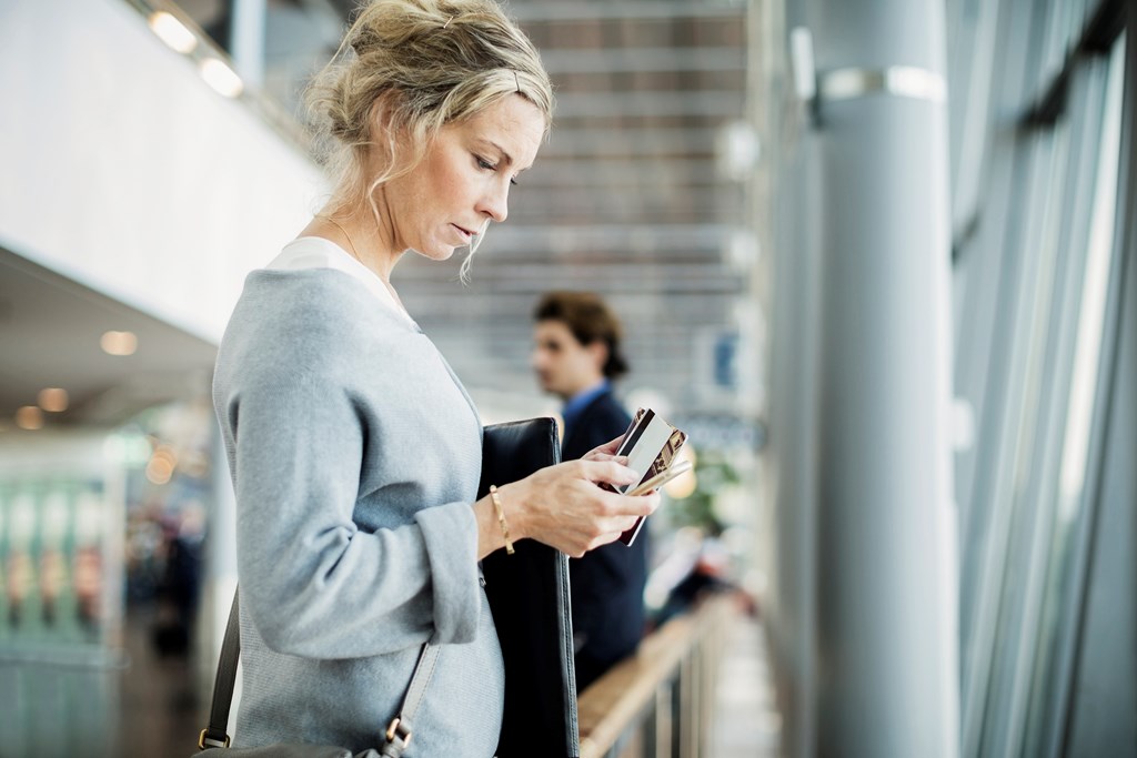 Nainen lentokentällä matkapuhelin kädessään